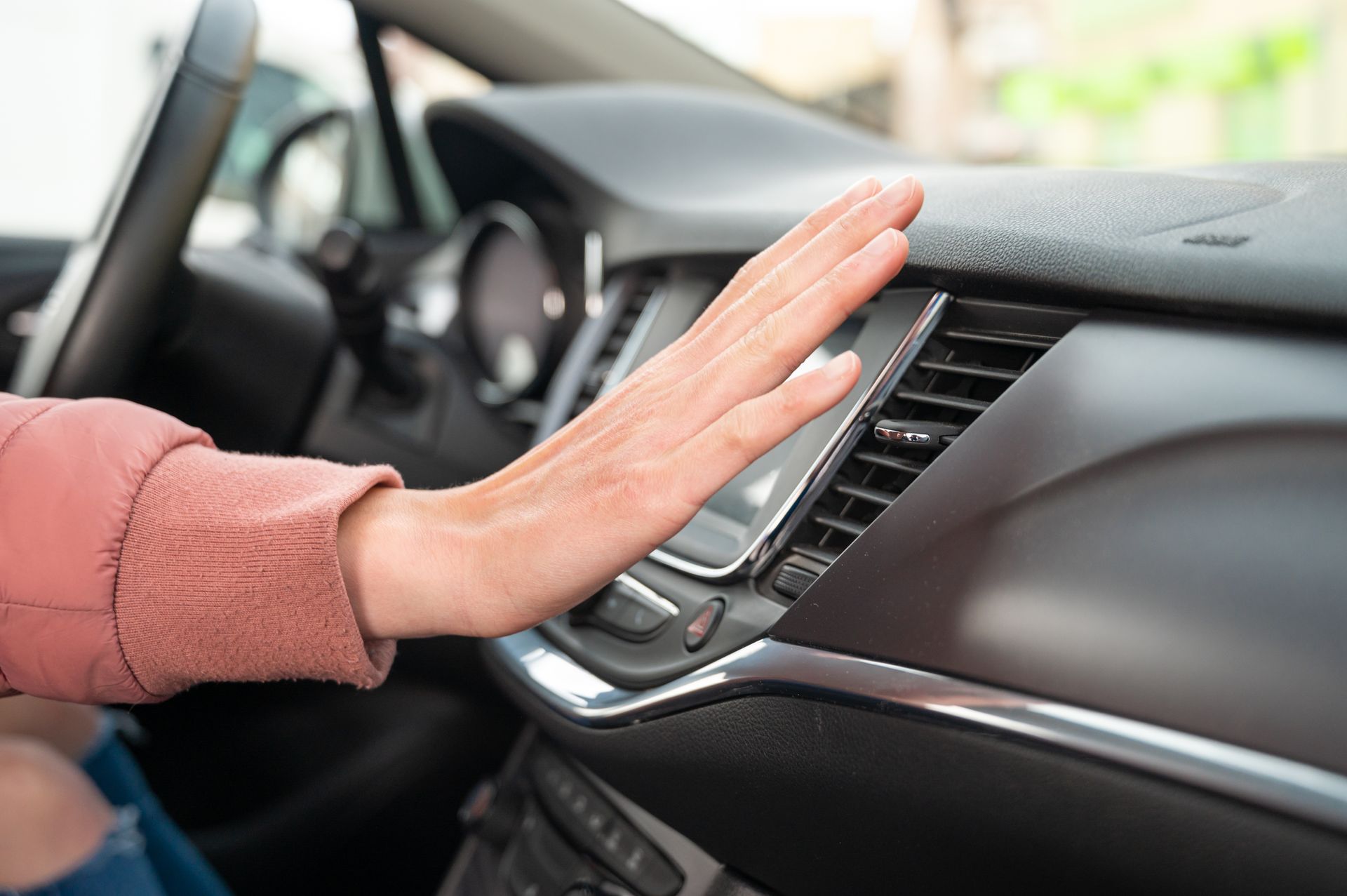 Hand pressing a car dashboard touchscreen next to air vents and center controls