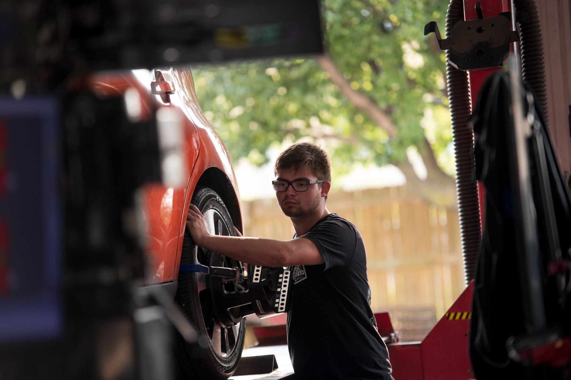 Mechanic working on a car wheel in an auto shop, with a vehicle lift and tools nearby