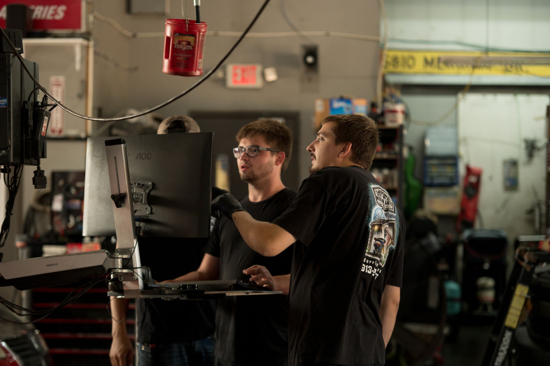 Two people working together at a machine in an auto repair shop, with tools and equipment around them