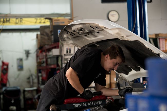 Mechanic working under a car hood in an auto repair shop