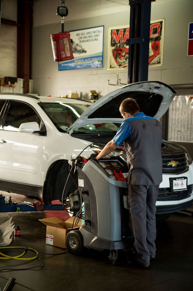 Mechanic working on a white SUV in an auto repair shop, hood open and diagnostic machine beside him