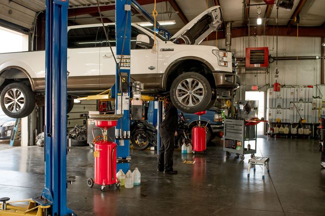 White SUV lifted in an auto repair shop with mechanics working underneath