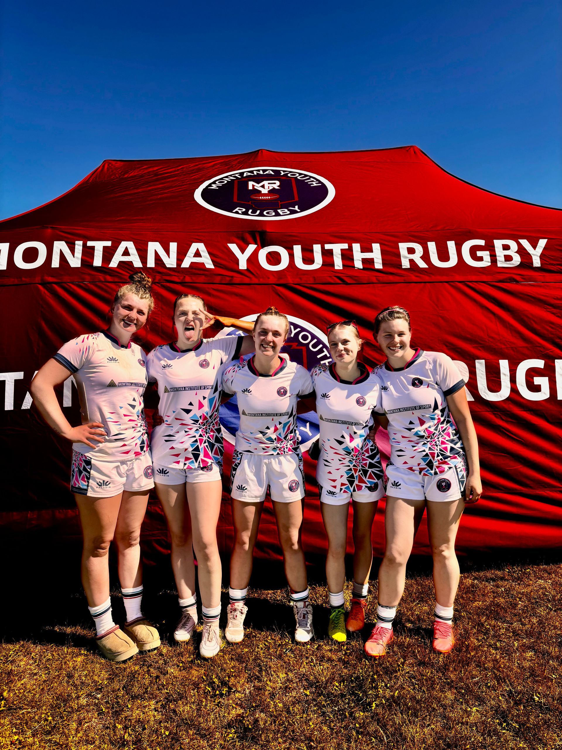 Six women in rugby uniforms pose in front of a 