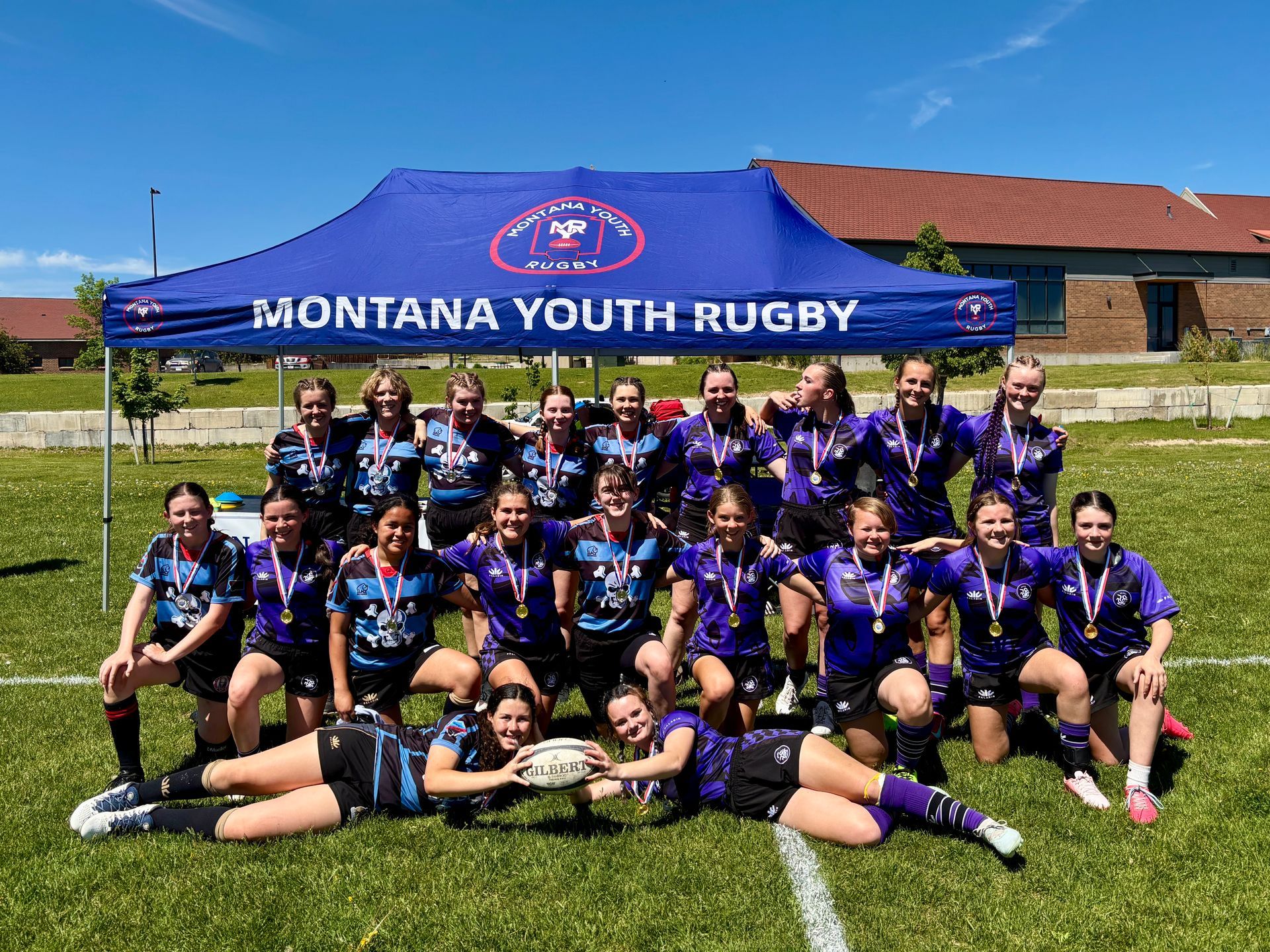 Montana Youth Rugby team poses with medals, wearing purple and black uniforms under a banner.
