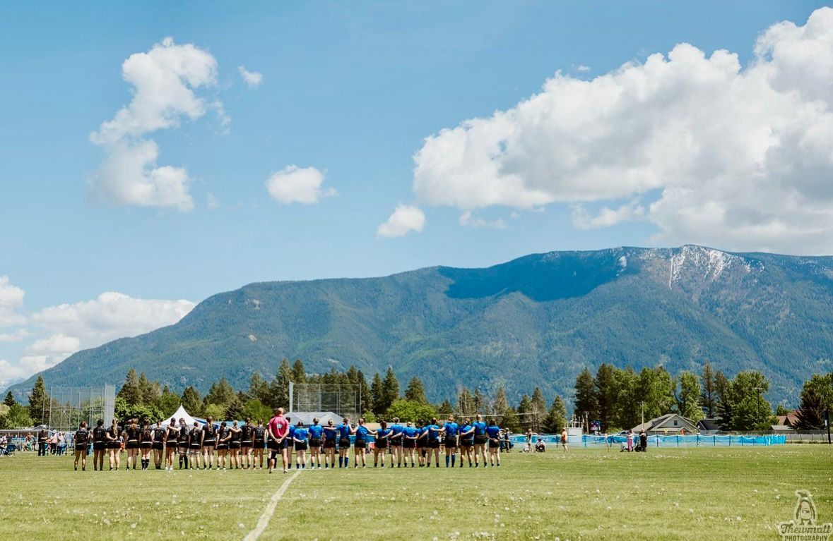 Teams lined up on a green field, with mountains and blue sky in the background.