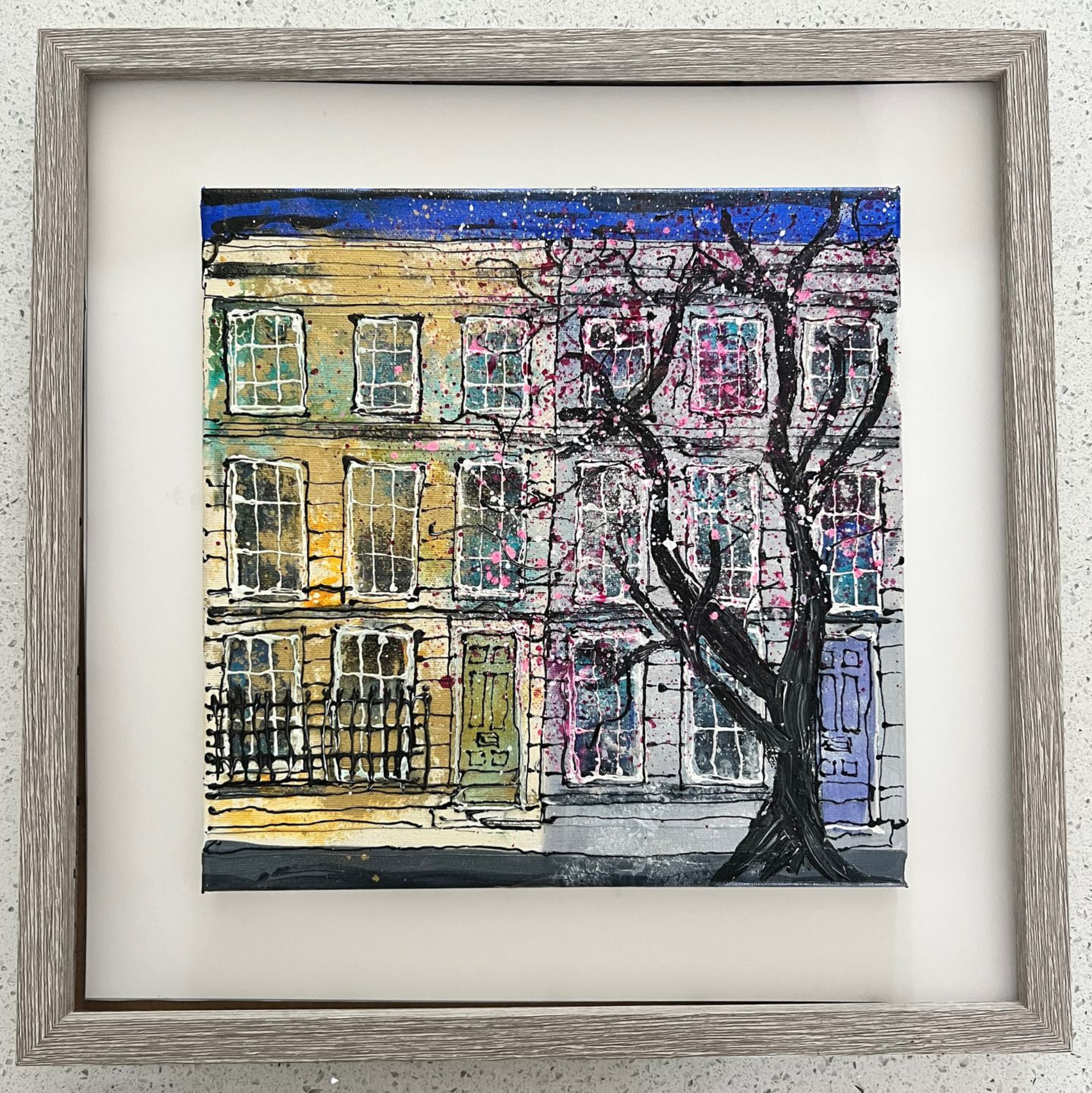 Colorful painting of a building with a tree in front. Yellow/purple building, blue sky, framed.