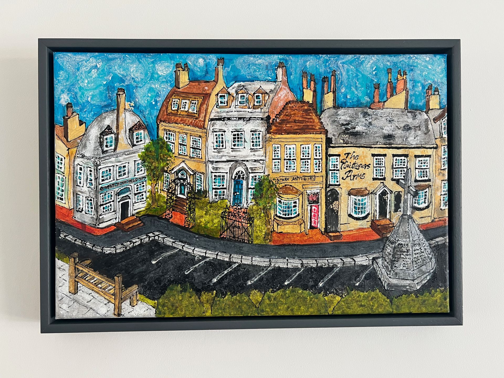 Colorful illustration of a row of buildings along a winding road, framed in black. Blue sky backdrop.
