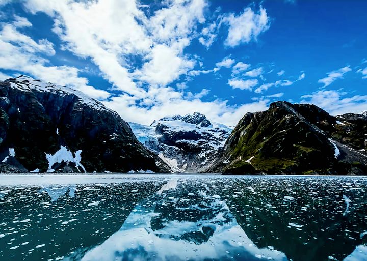 Snow-covered mountains and glacier behind a blue lake under a clear sky