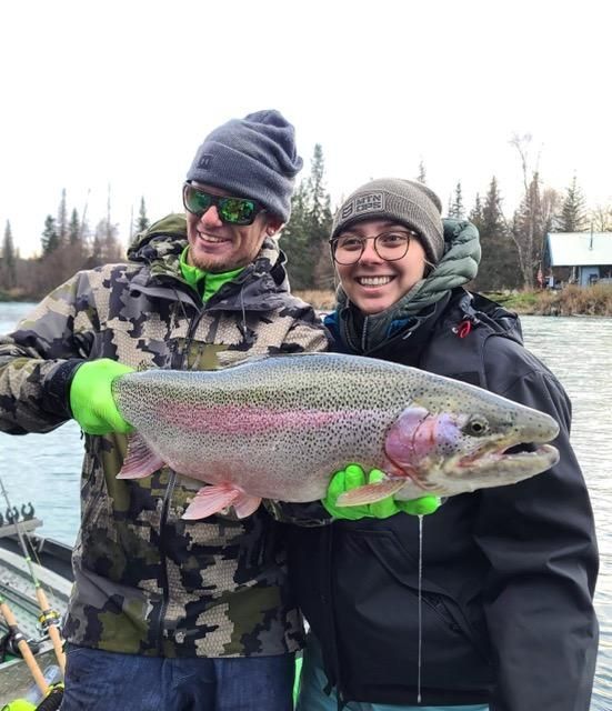 Two people in winter gear holding a large rainbow trout outdoors.