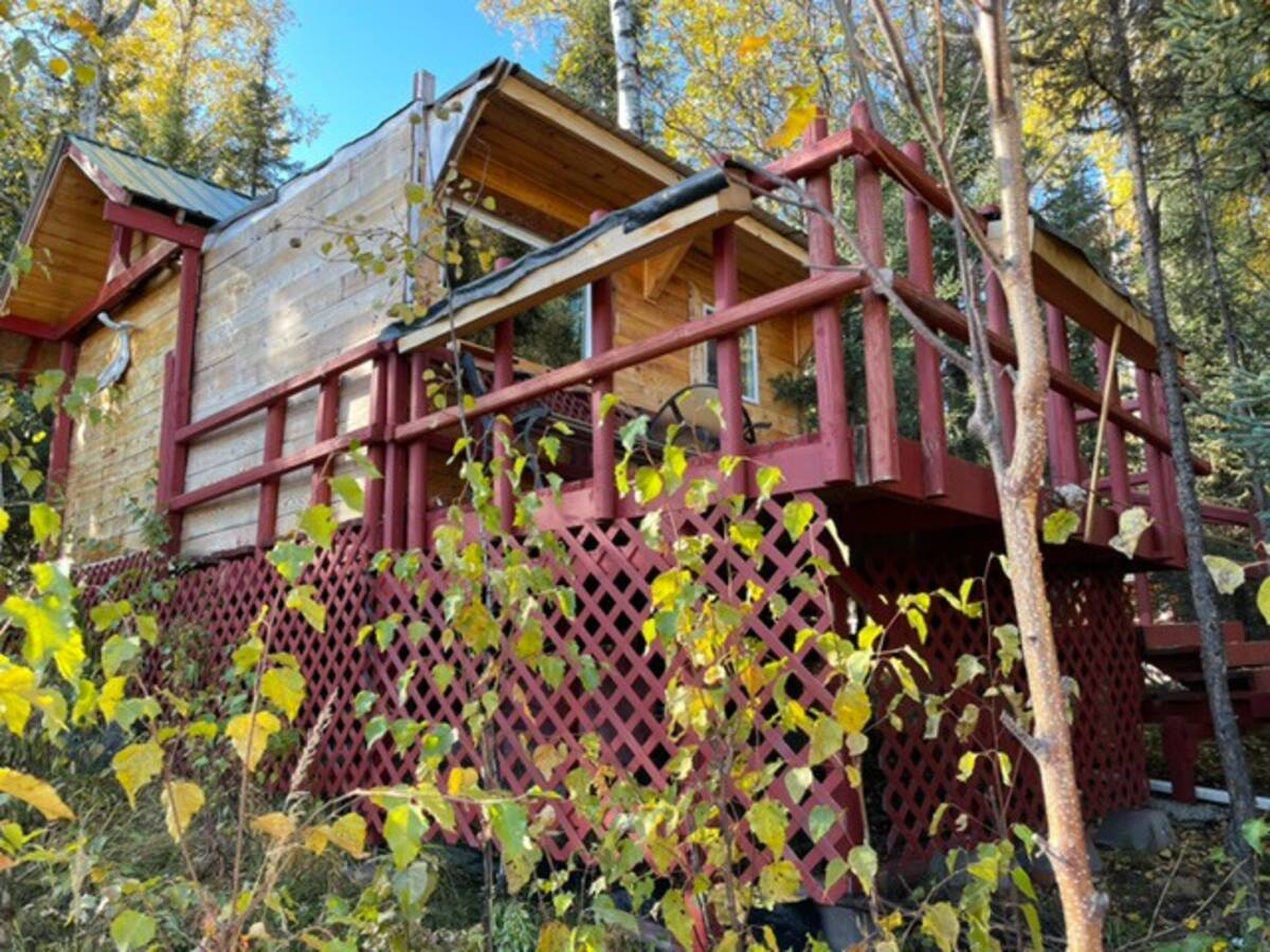 Red cabin with porch and lattice railing on a wooded hillside in autumn