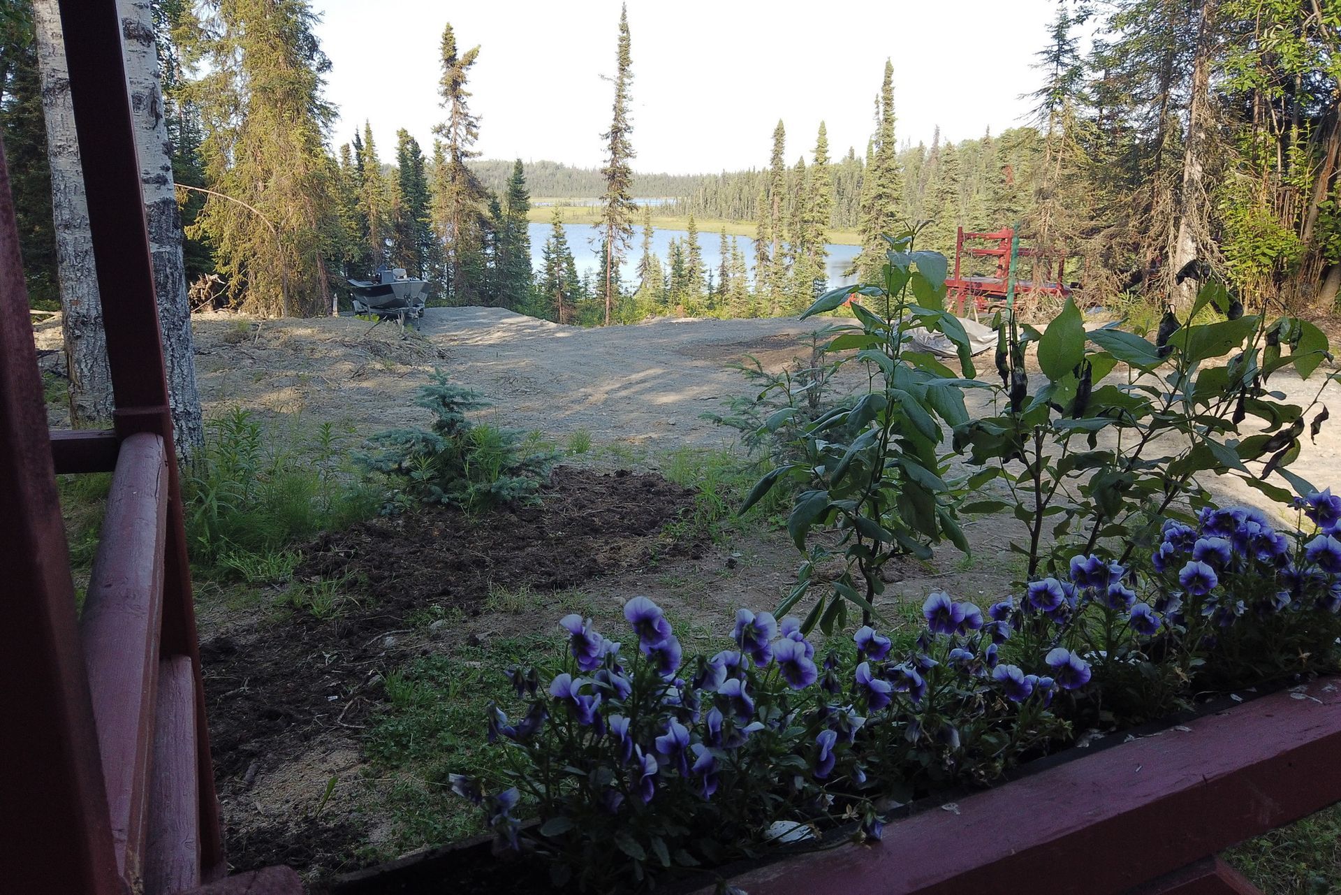 Flowering garden overlooking a lake, with trees and a porch railing in the foreground