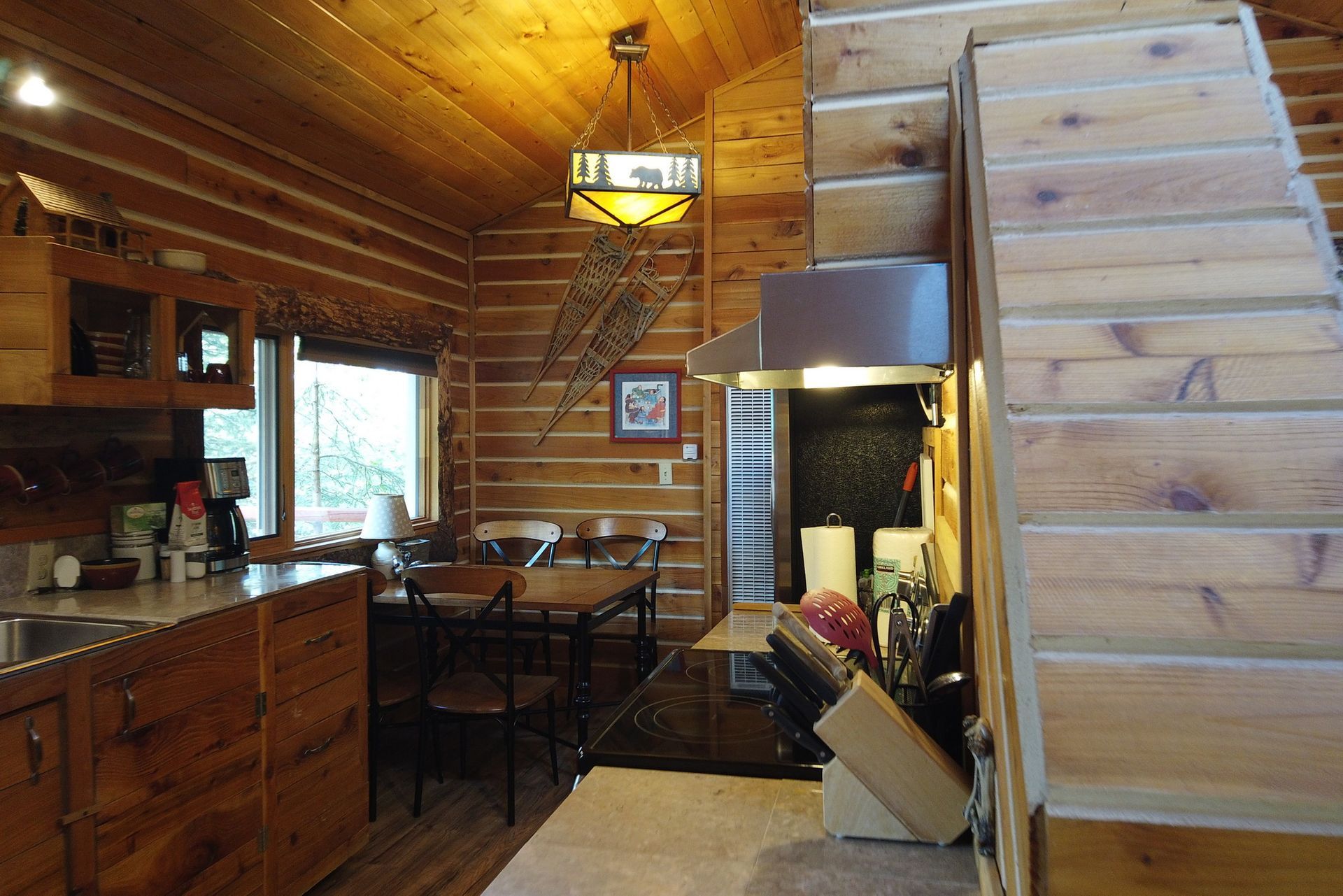 Cozy wooden cabin interior with kitchen, dining table, and staircase.