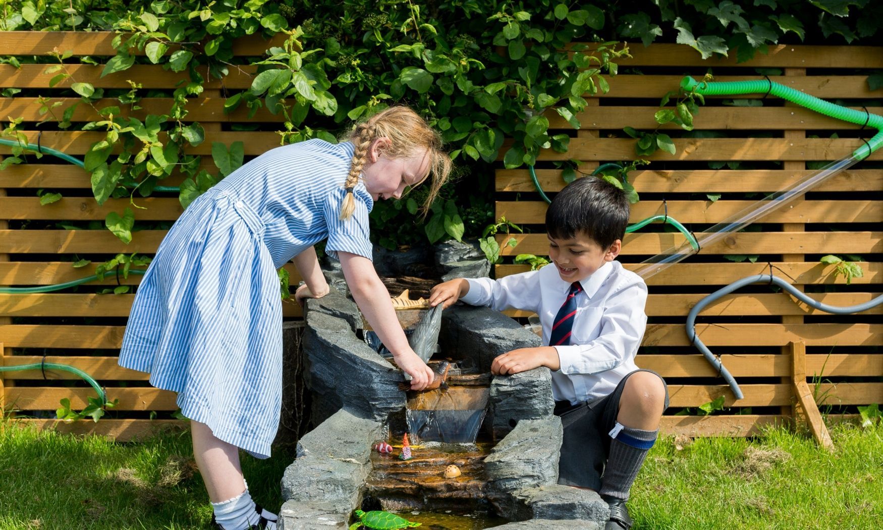 A boy and a girl are playing with a water fountain.