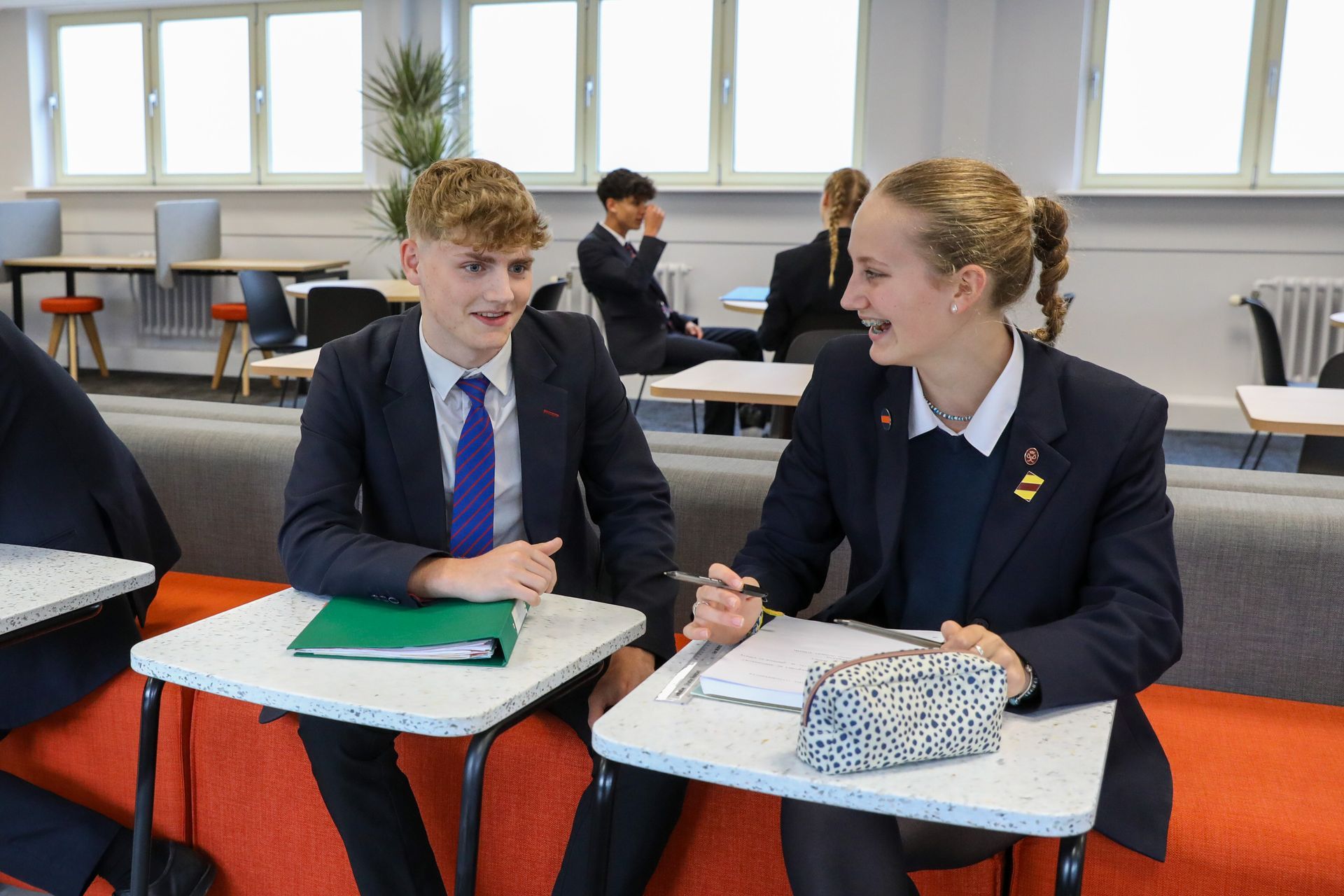 A boy and a girl are sitting at desks in a classroom.