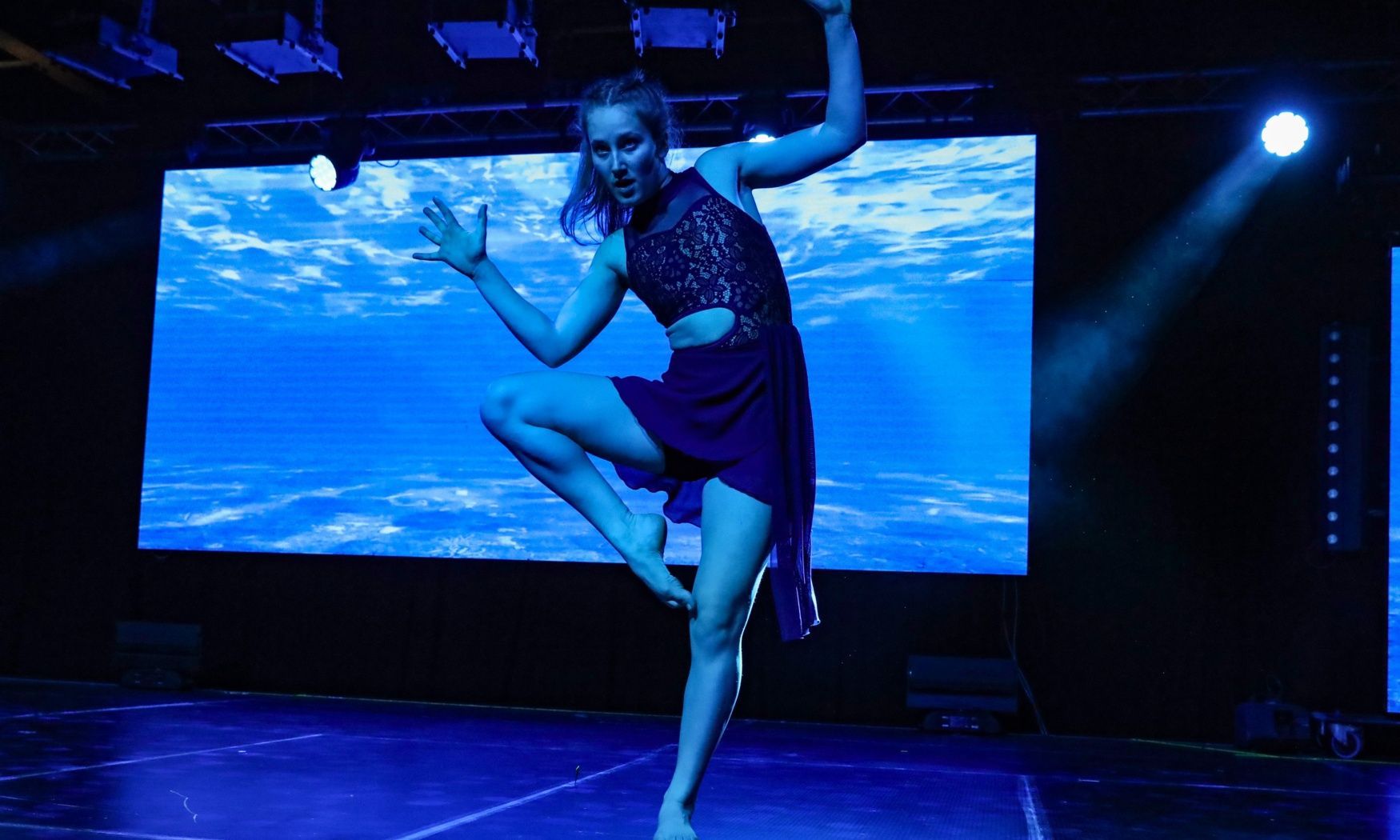 A woman is dancing on a stage in front of a large screen.
