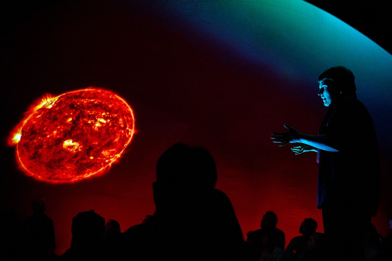 A man stands in front of a projection of the sun