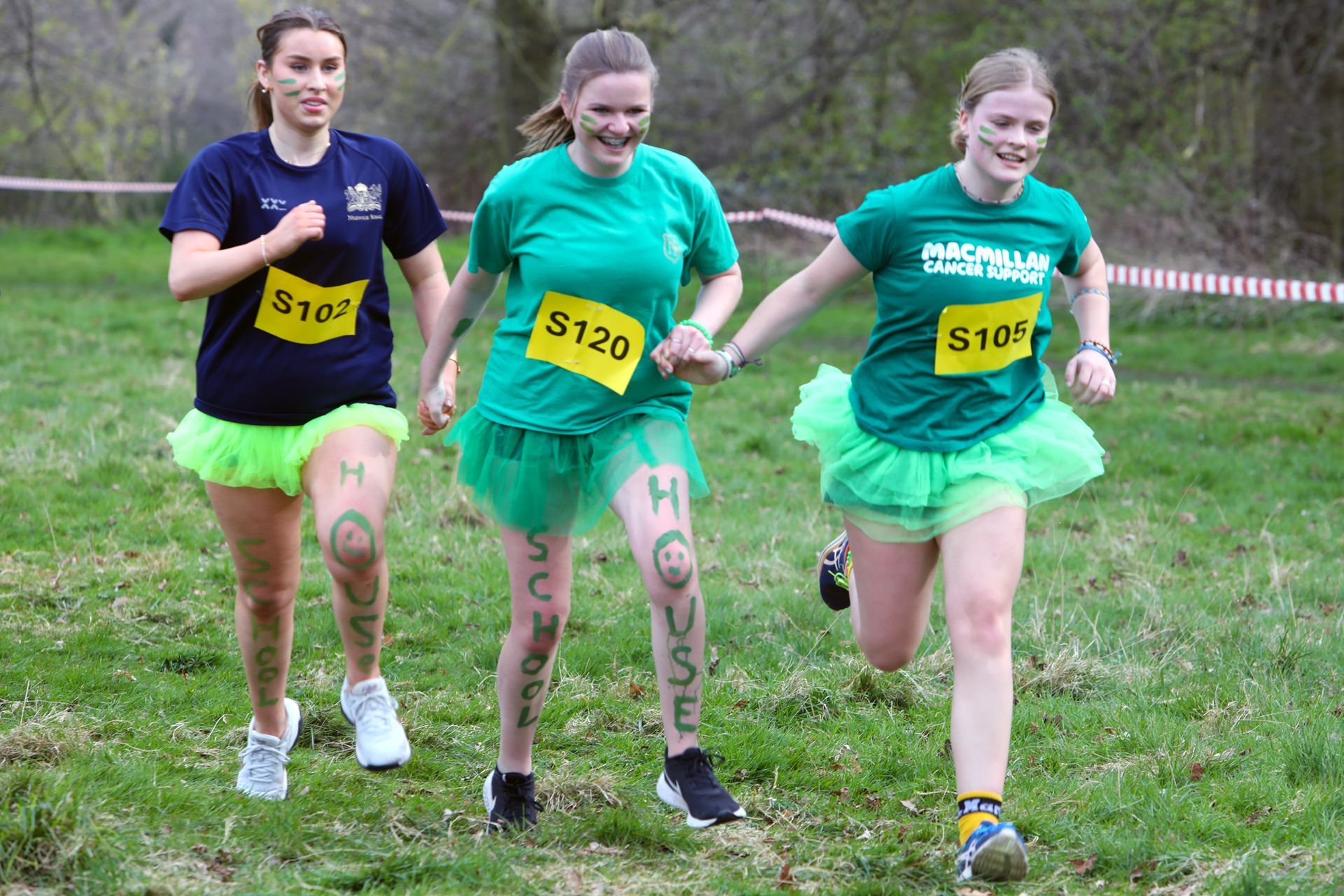 Three women are running in a field and one has the number s120 on her shirt