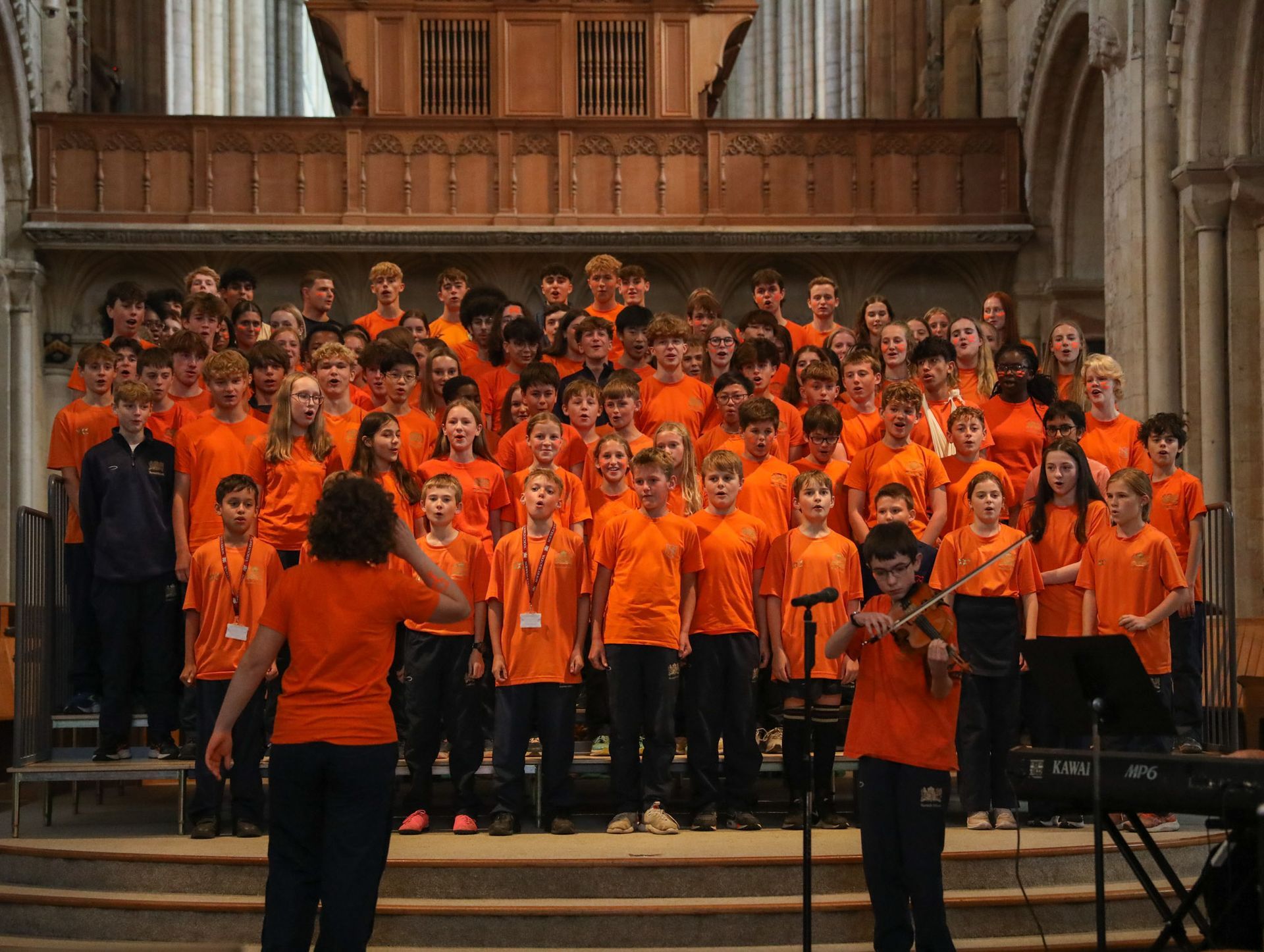 A large group of children in orange shirts are singing in a church
