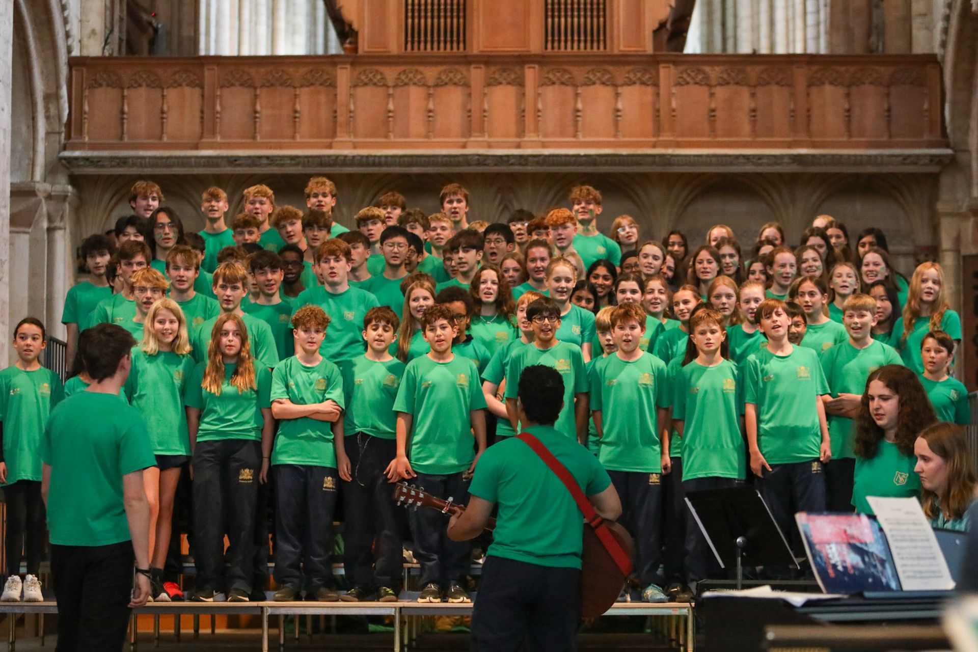A man is playing a guitar in front of a large choir.