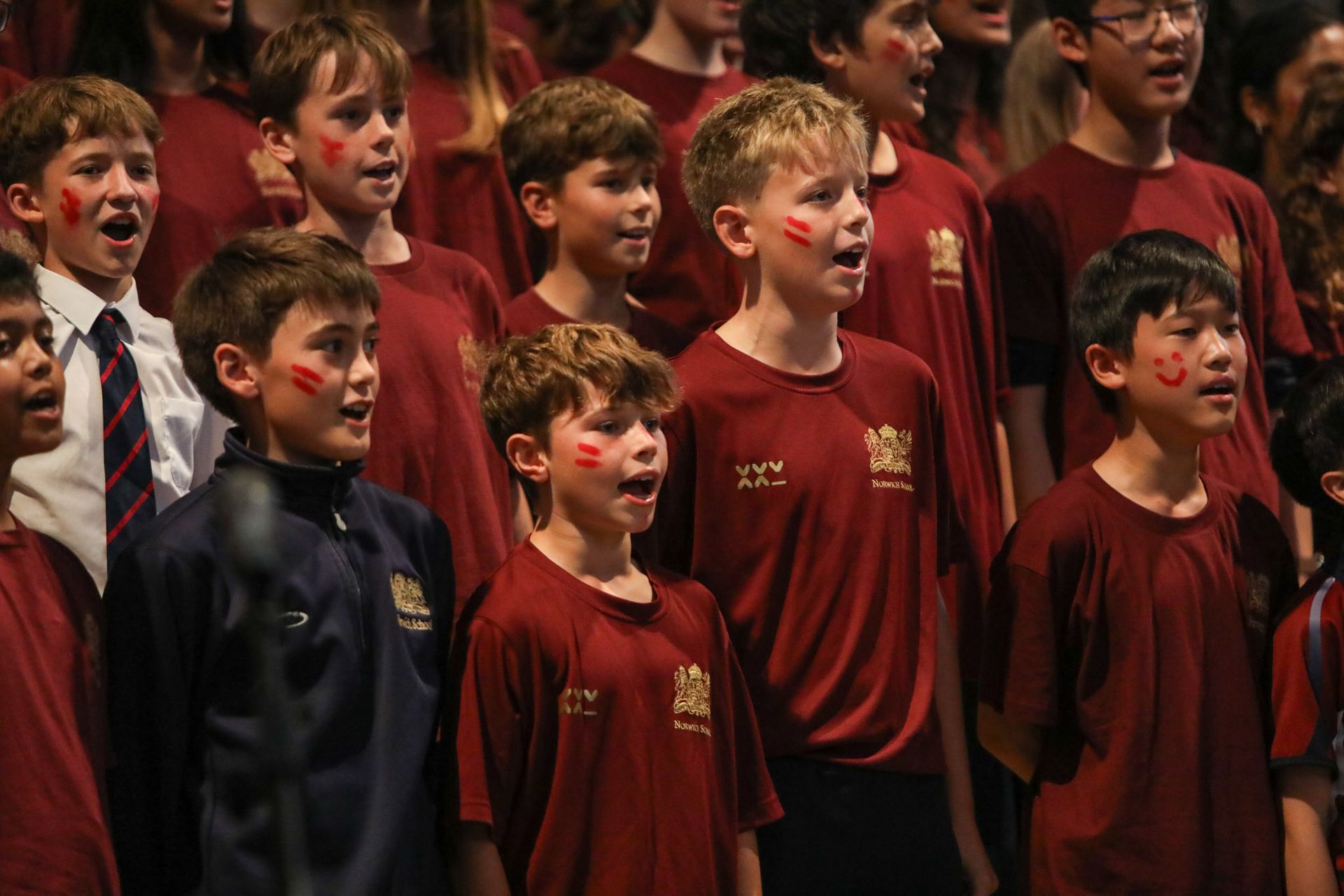 A group of young boys in red shirts are singing in a choir.