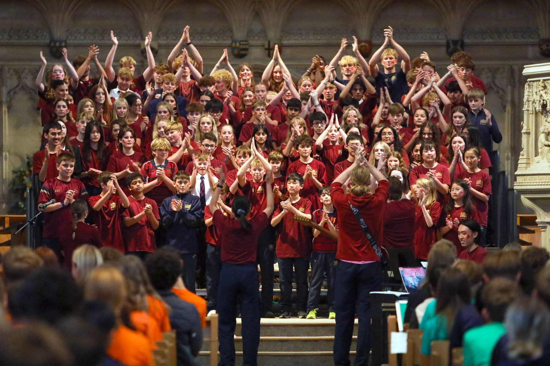 A large group of people are standing in a church with their hands in the air.