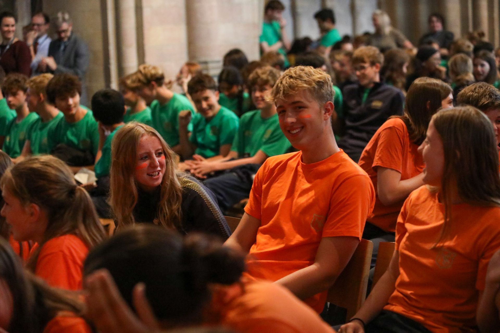 A group of people wearing orange shirts are sitting in a room.