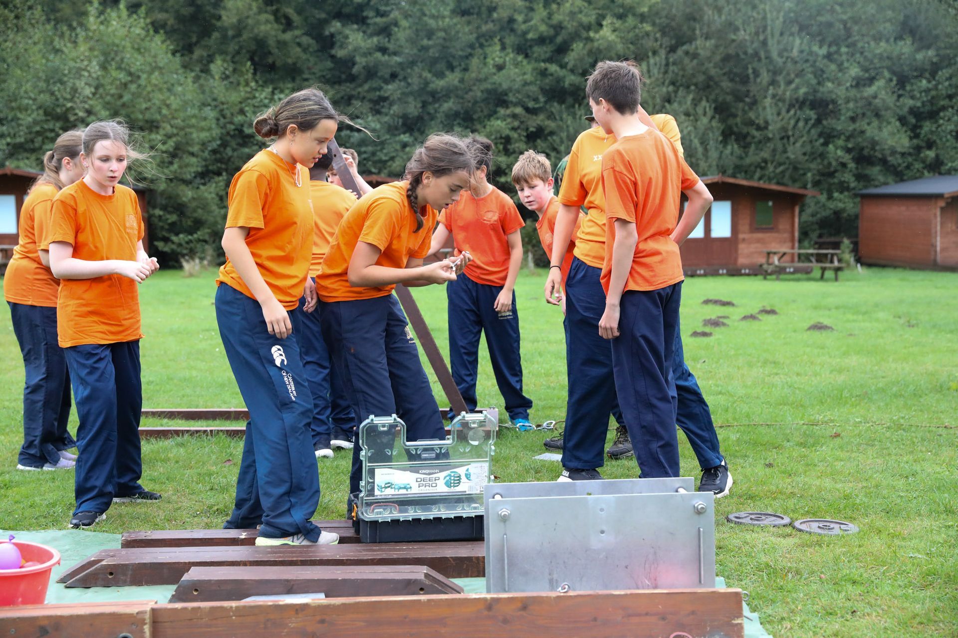A group of children in orange shirts are working on a wooden structure.