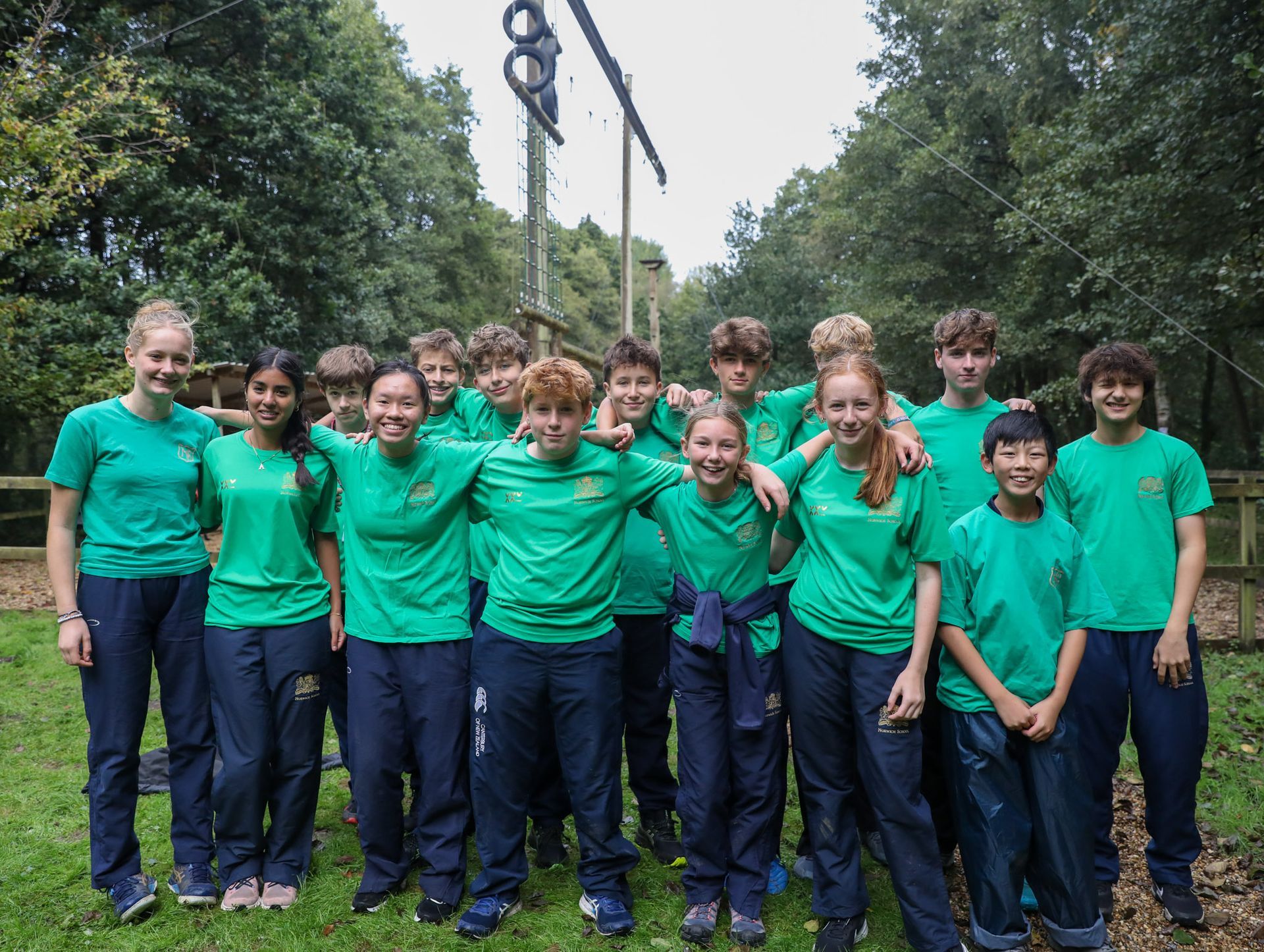 A group of young people wearing green shirts and blue pants are posing for a picture.