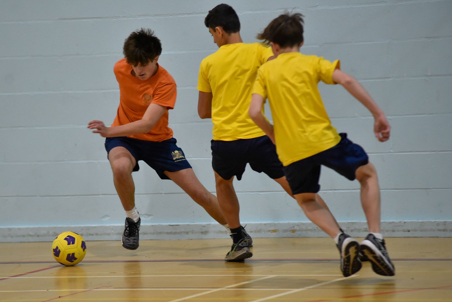 Three boys in yellow shirts are playing soccer on a court