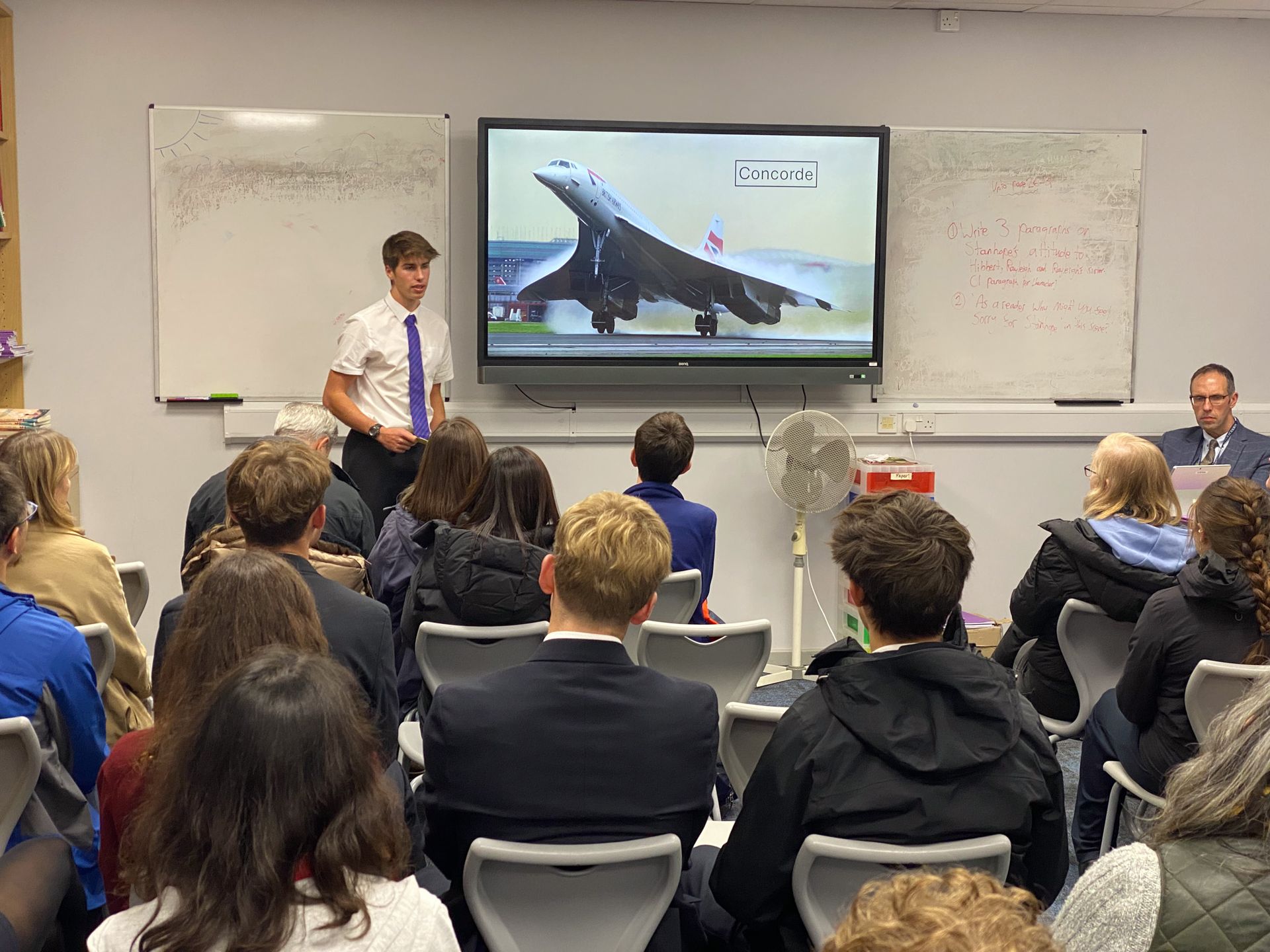 A man is giving a presentation to a group of people in a classroom.