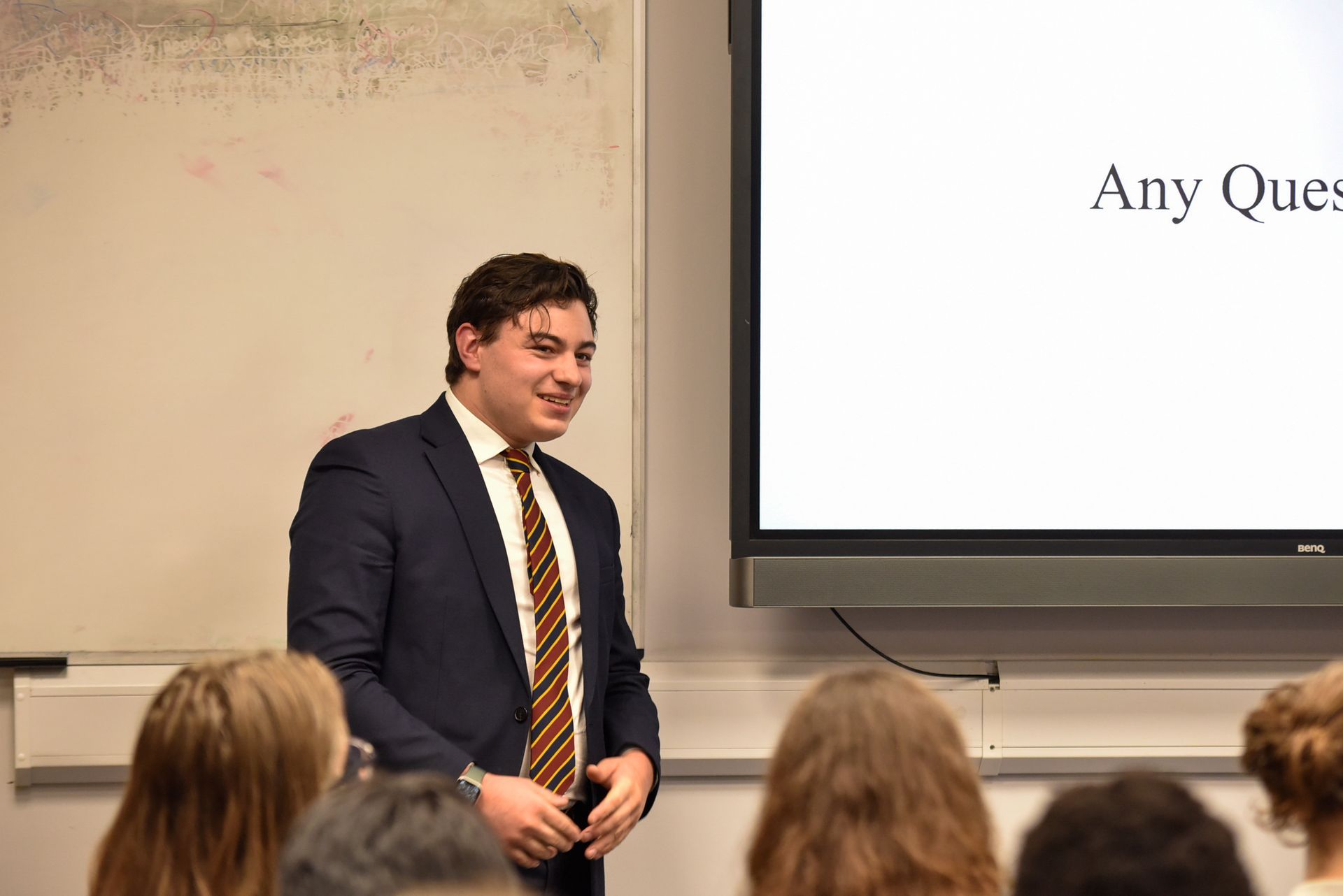 A man in a suit and tie is giving a presentation to a group of students.