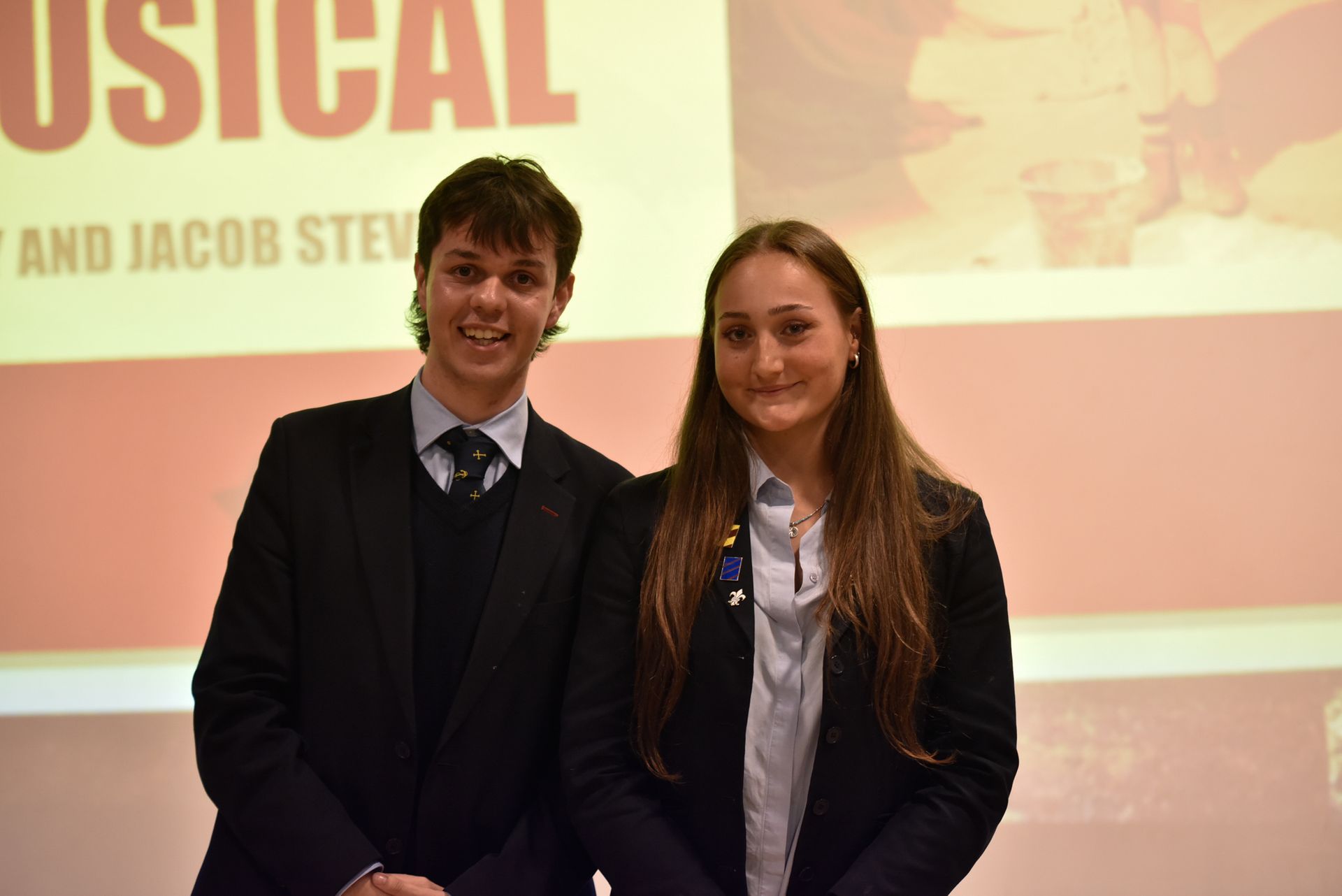 A man and a woman are posing for a picture in front of a screen that says musical