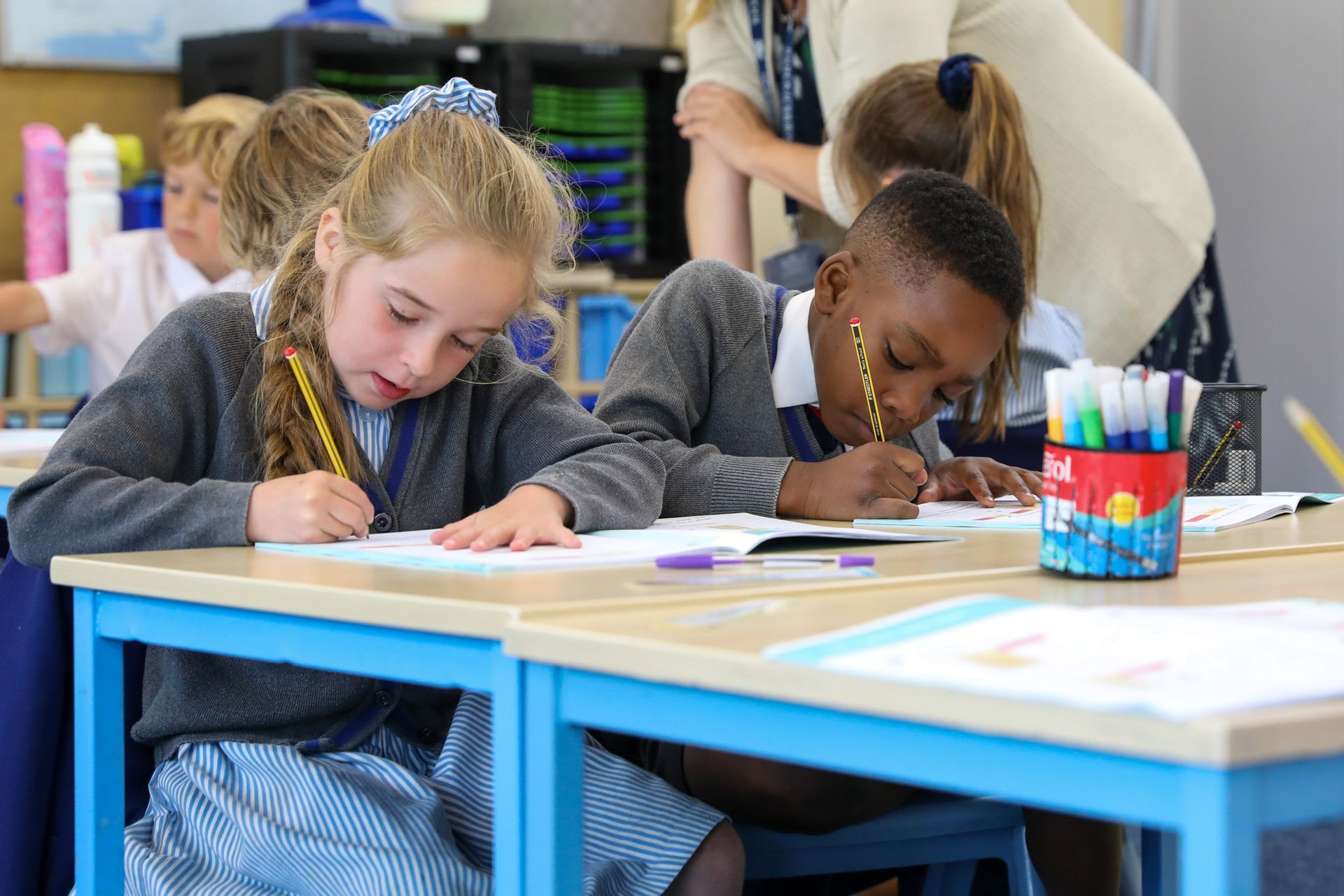 Two young boys are sitting at desks in a classroom using tablets.