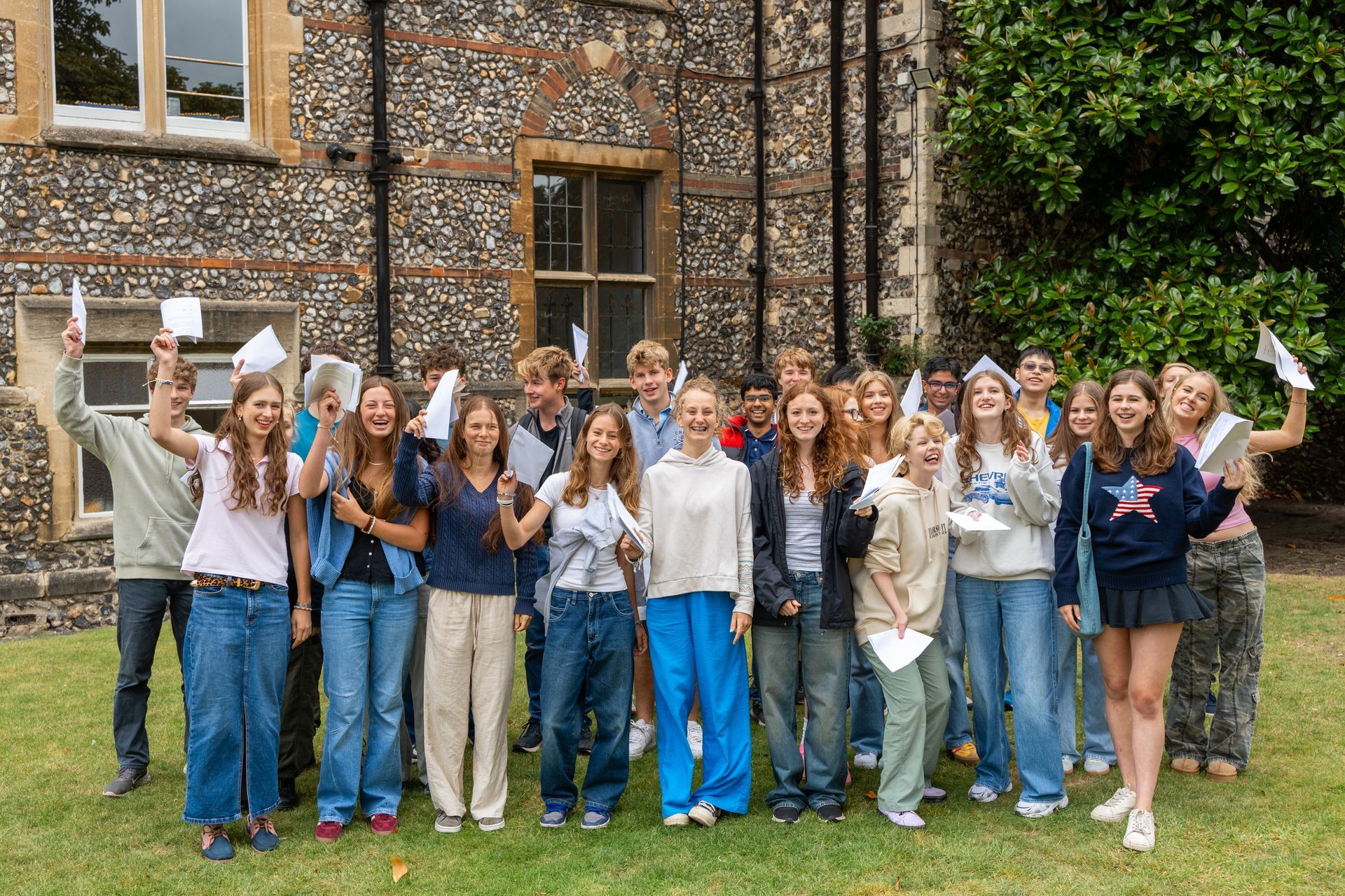 A group of young people are standing in front of a stone building holding up papers.
