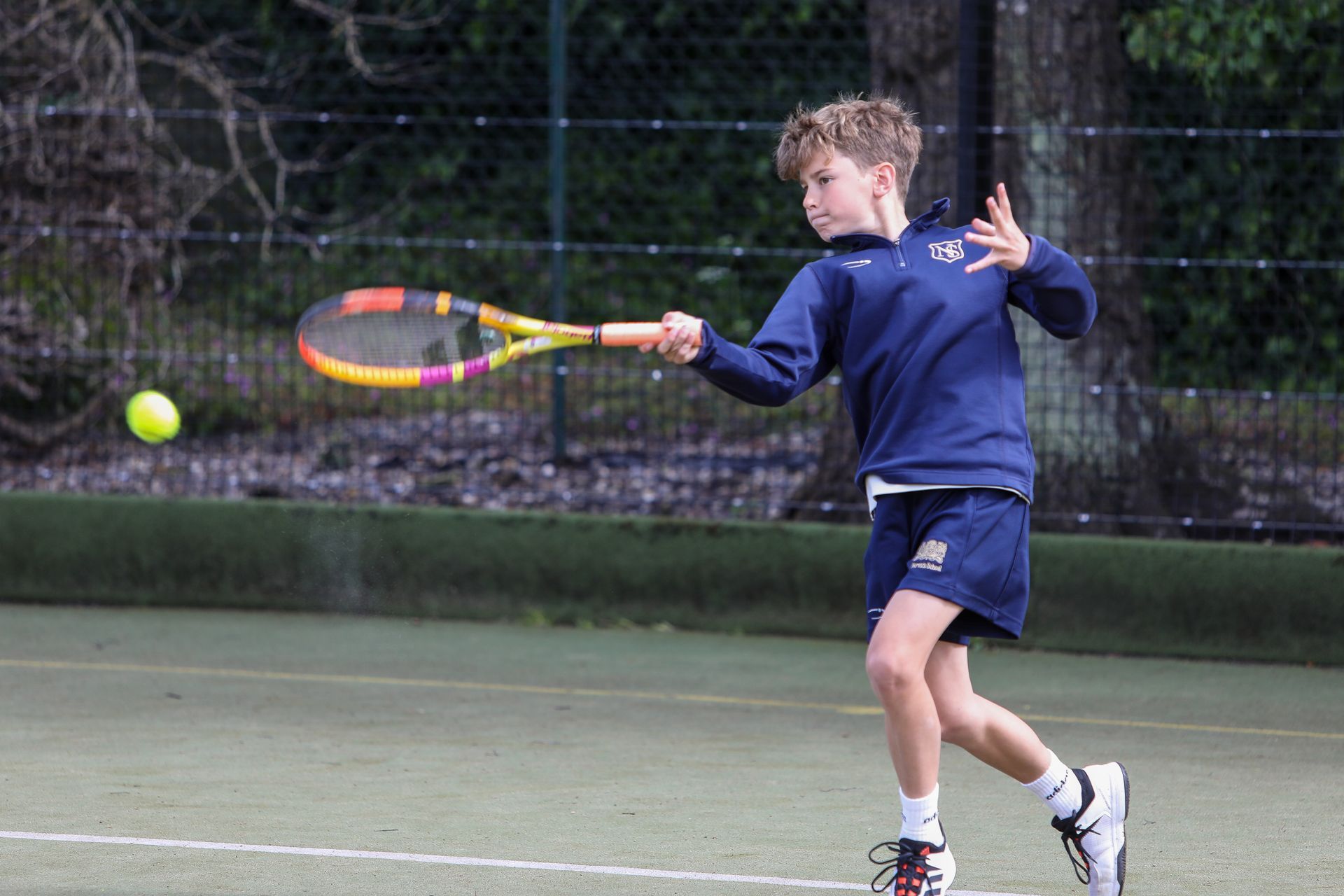 A young boy is playing tennis on a tennis court.