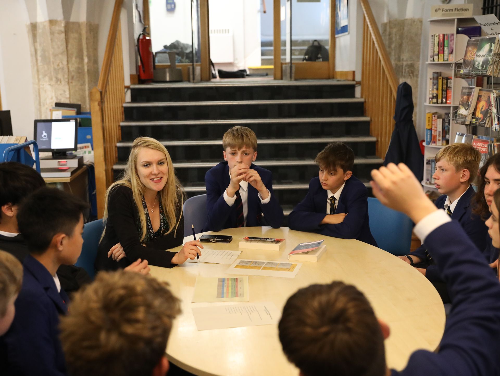 A group of pupils are sitting around a table with their hands up