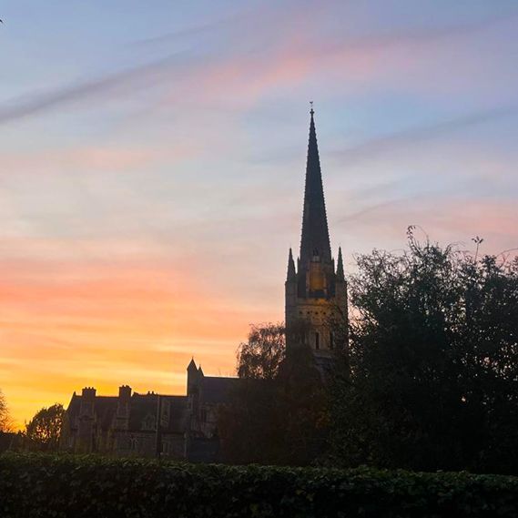 A church with a steeple is silhouetted against a sunset sky.