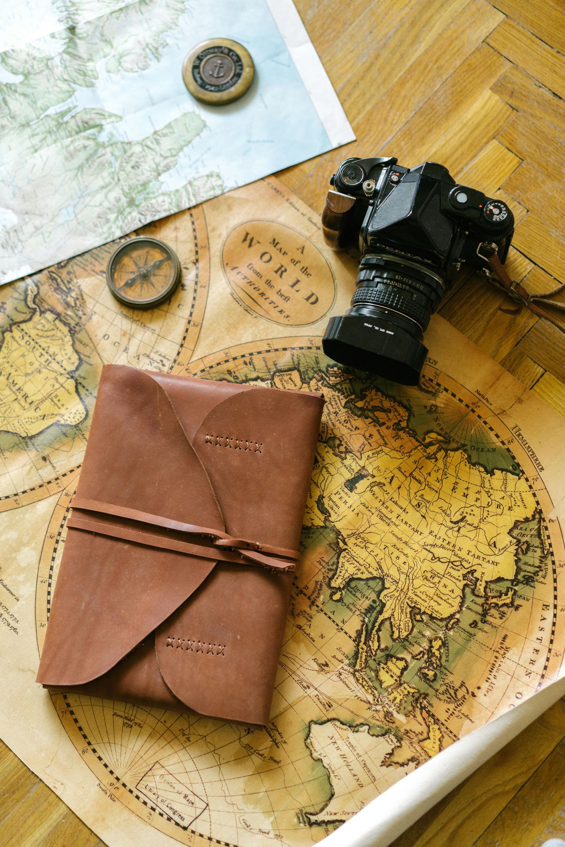 A leather wallet is sitting on top of a map next to a camera and compass.
