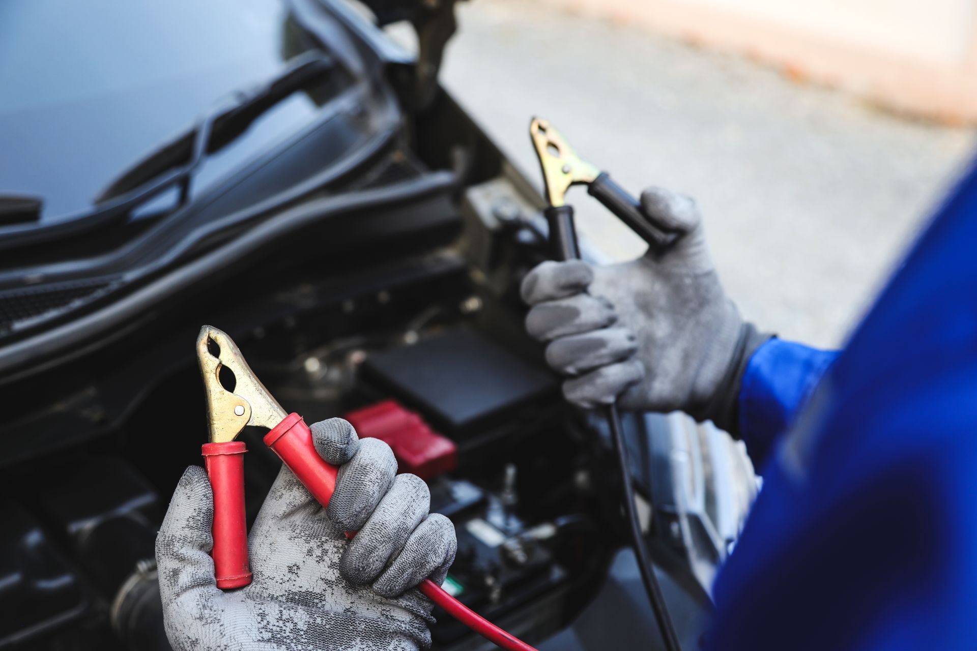 A person is holding a pair of jumper cables in front of a car.