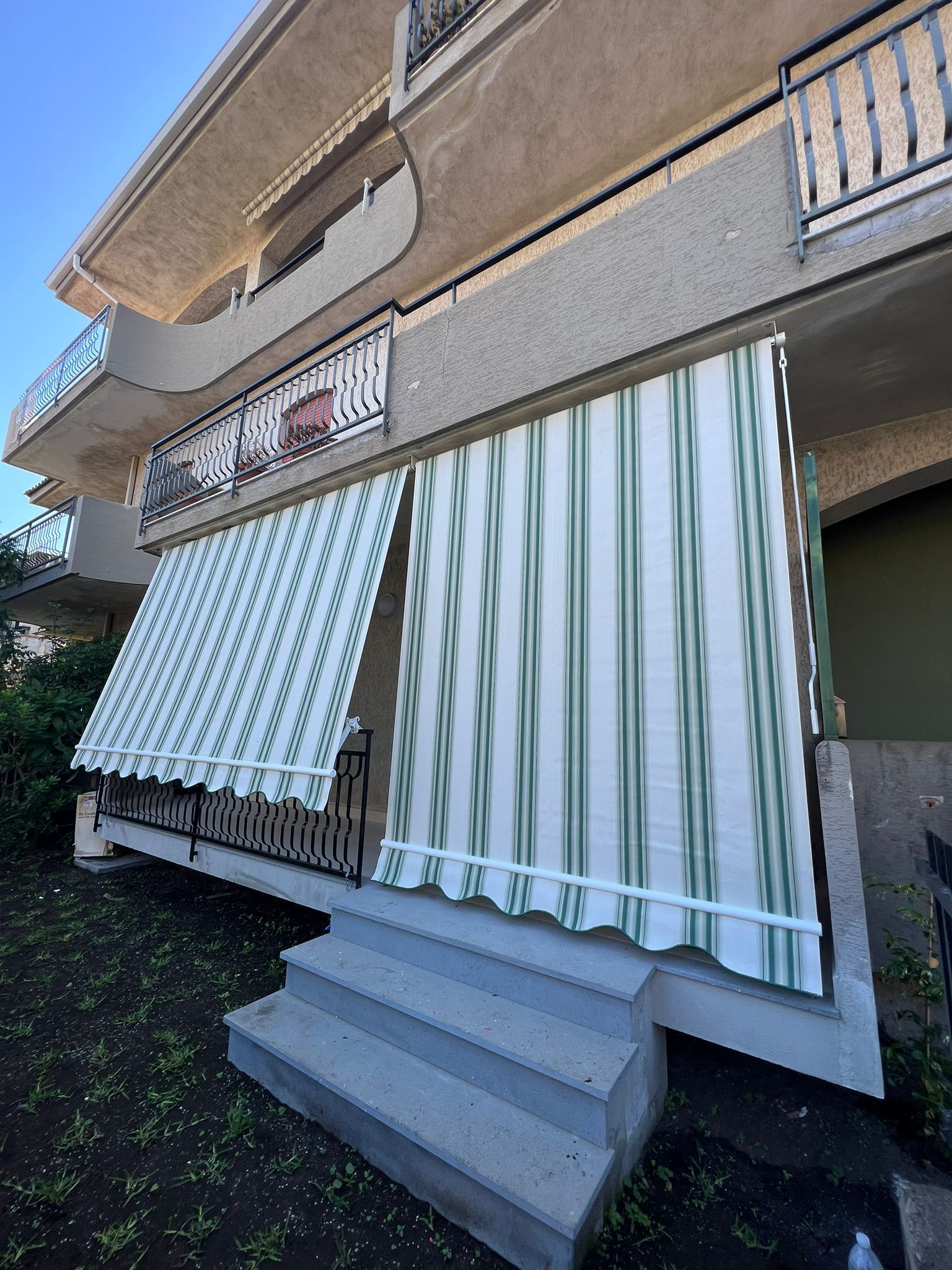 Balcone dell'appartamento con tenda da sole a righe verdi e bianche e ombrellone decorato sopra i gradini.
