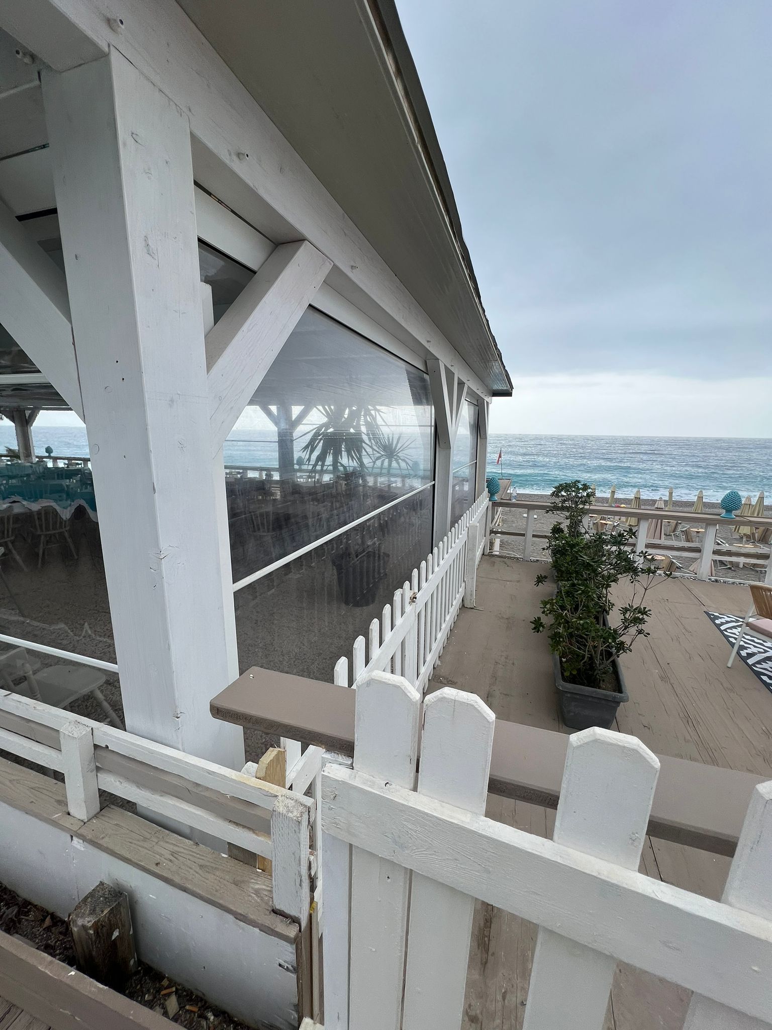 Patio sul mare con ringhiere e pali bianchi che si affacciano sull'oceano in una giornata di sole.