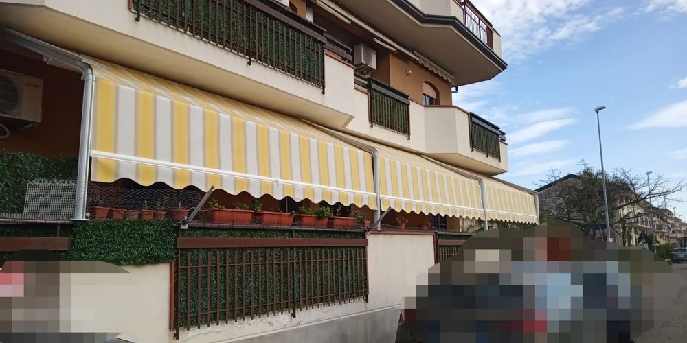 Tenda a strisce gialle e bianche sulla facciata di un edificio, accanto a un'auto parcheggiata sfocata e al marciapiede.