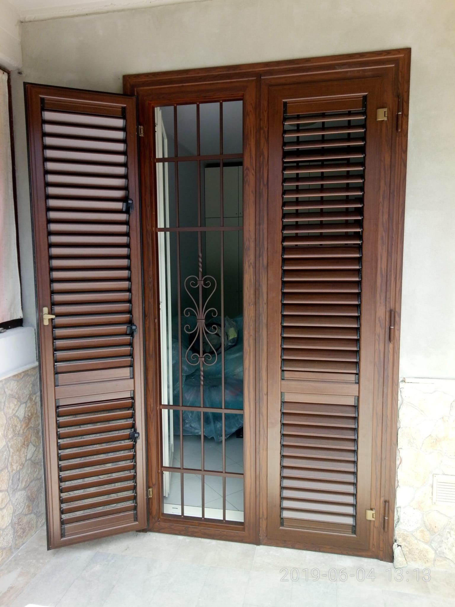 Porta in legno marrone con persiana, grata di sicurezza in metallo e pannelli in vetro satinato.