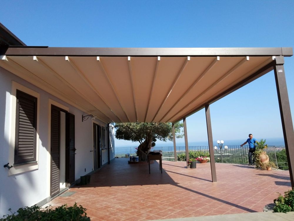 Patio coperto con pavimento in terracotta, parete bianca della casa e vista sull'oceano in lontananza sotto un cielo luminoso