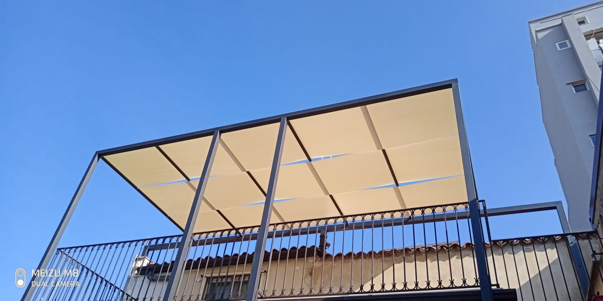 Balcone con ringhiera in metallo e baldacchino beige contro un cielo azzurro limpido.