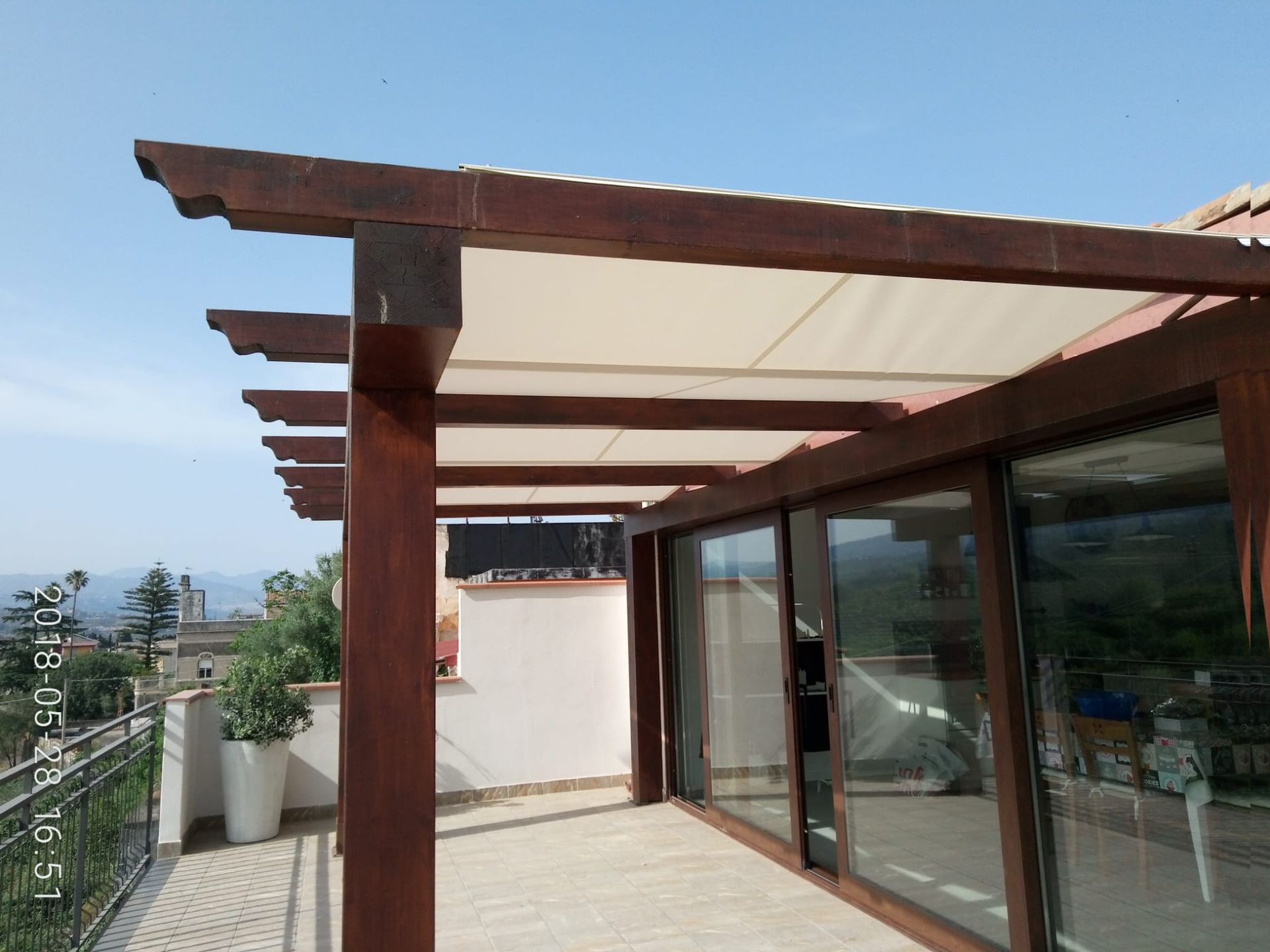 Terrazza esterna con pergola in legno, porte scorrevoli in vetro e vista mare.