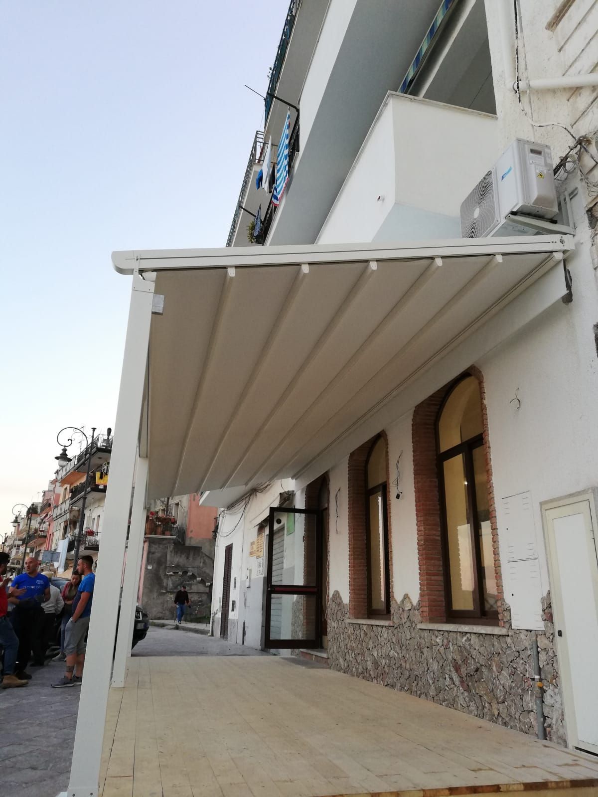 Tenda bianca sopra l'ingresso di un edificio su una strada stretta, con muri in pietra e finestre ad arco.