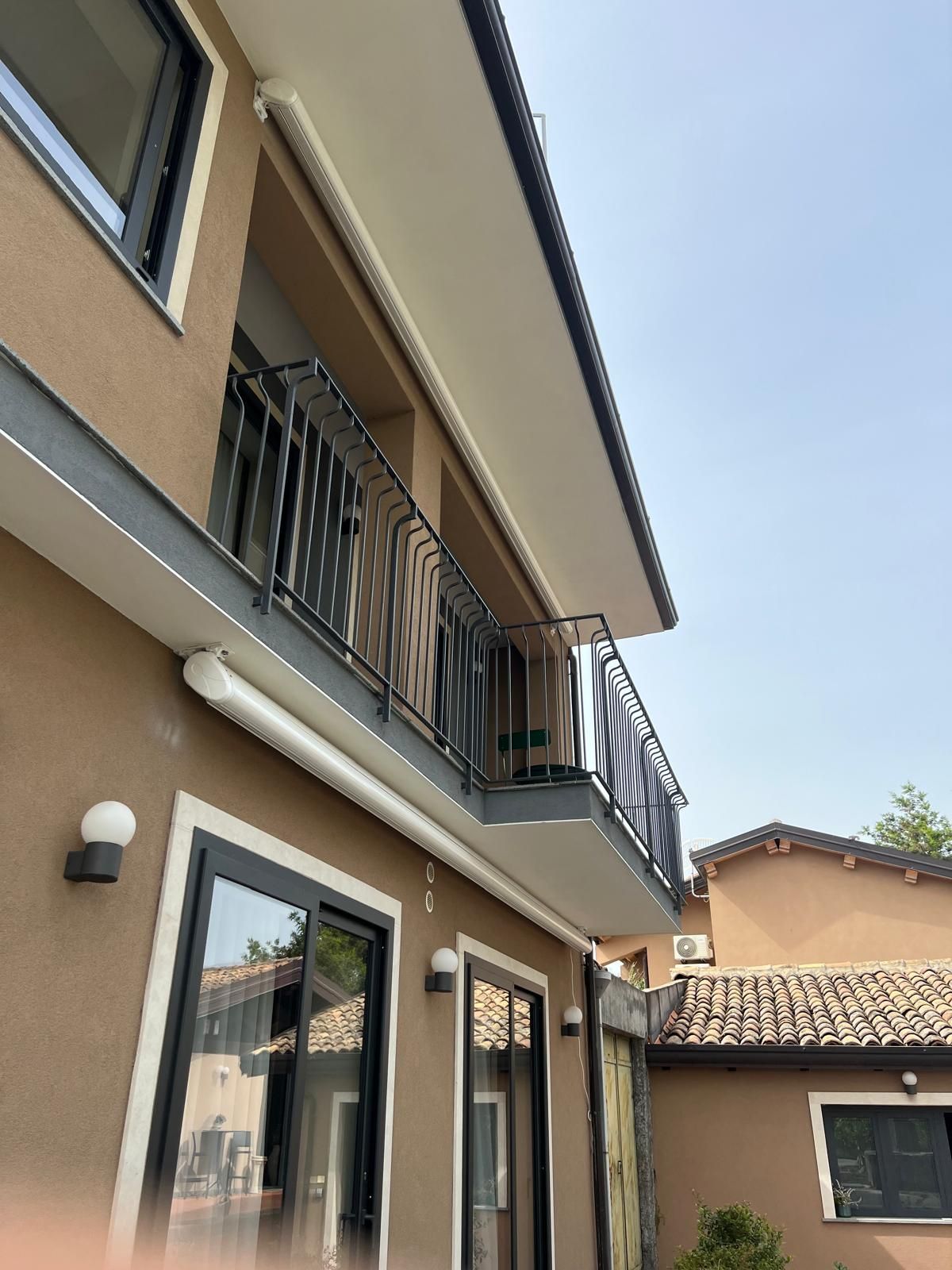 Casa a schiera beige su due piani con balconi e porte scorrevoli in vetro sotto un cielo limpido