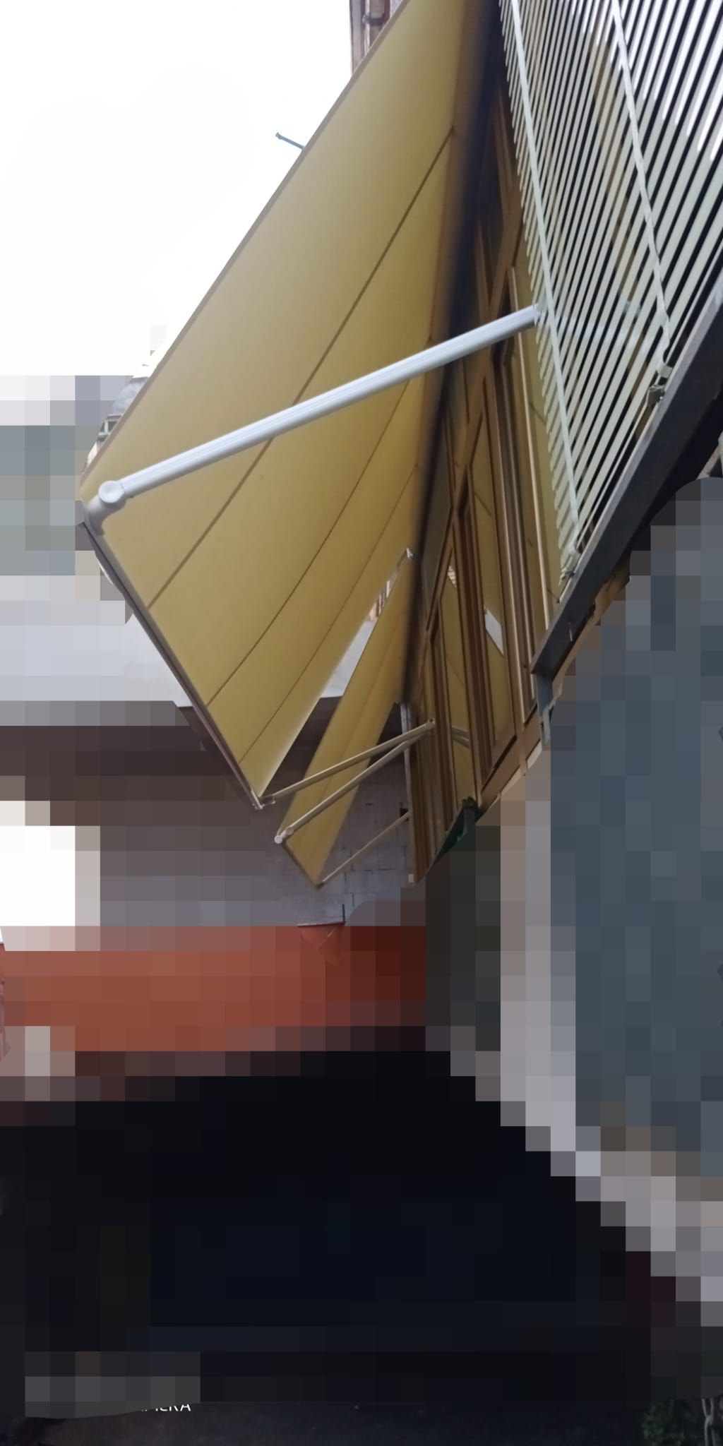Primo piano di una tenda da sole in metallo beige con bracci di supporto accanto alla facciata di un edificio.