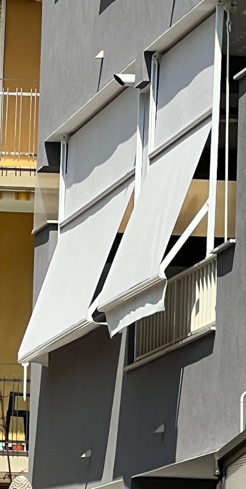 Finestre dell'appartamento con tende da sole bianche parzialmente estese sulla facciata grigia dell'edificio.